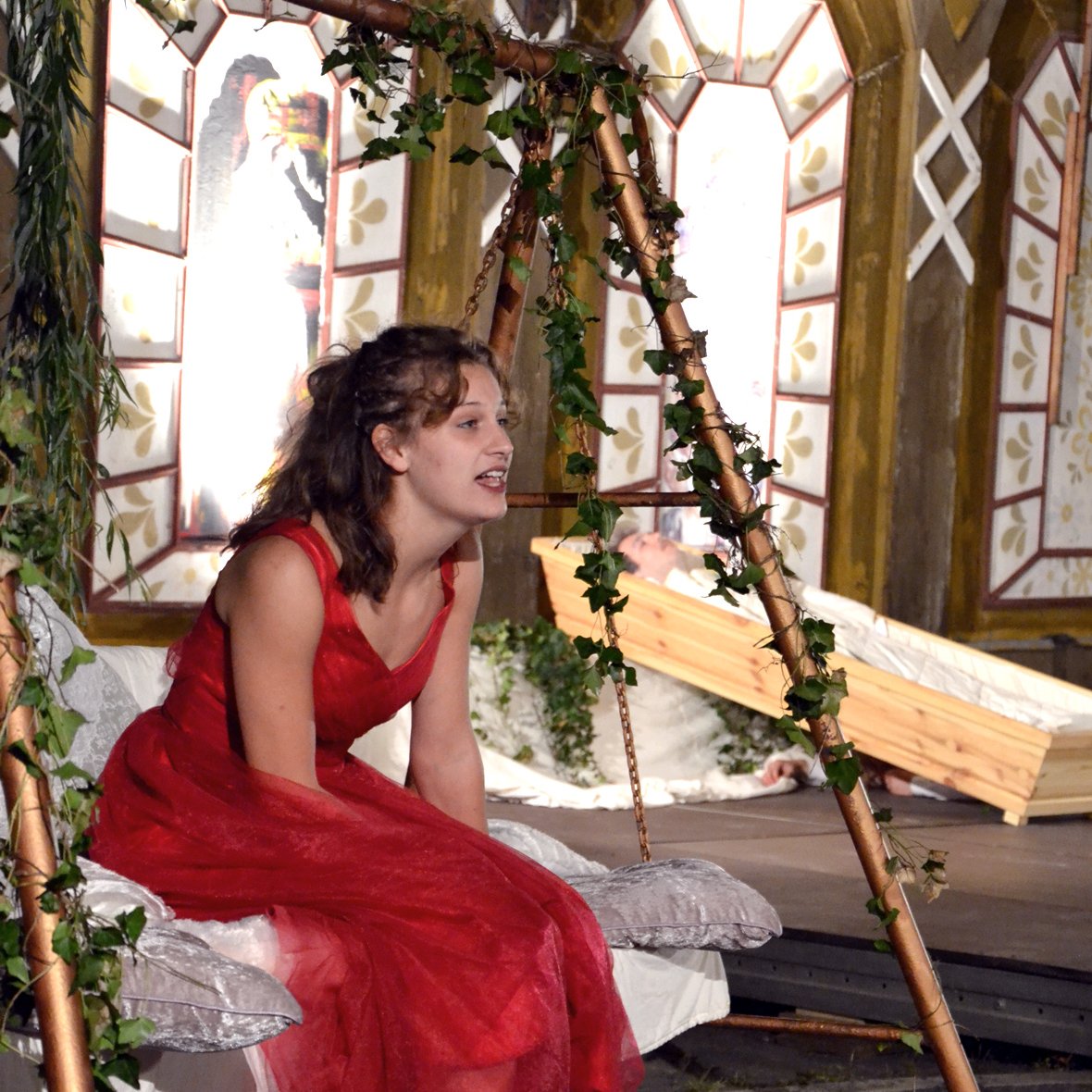 Schauspielerin in rotem Kleid sitzt auf einer Schaukel in einem Schloss