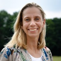 Katja Kramarczyk unter blauem Himmel mit einer grau-braunen Weste mit bunten Pflanzen aufdrucken