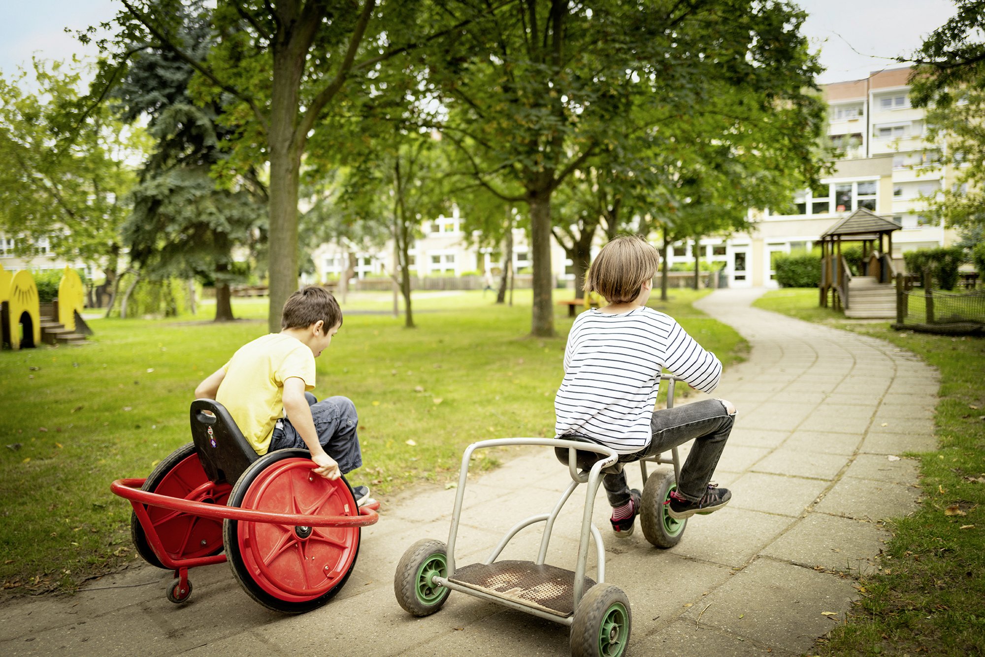 zwei Kinder fahren mit Dreirädern über einen Weg 