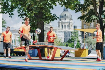 zusehen sind Junge Menschen die mit einem Fußball auf einer Tischtennisplatte spielen 