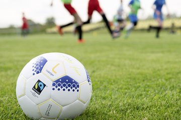 zusehen ein Fußball auf einem Rasenplatz, Hintergrund Menschen die trainieren 