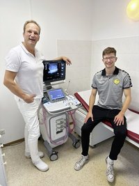 Kapitän der SG-Olympia sitzt lachend auf der Liege im Artzimmer bei Dr. Conrad Kubel