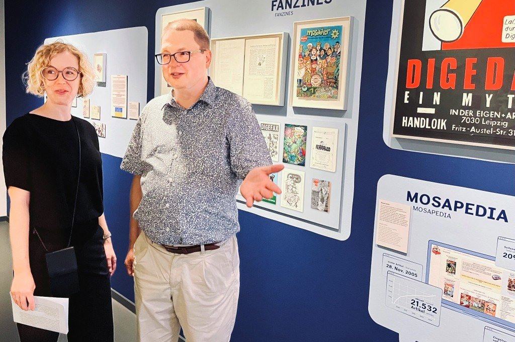 Direktorin Uta Brettschneider und Michael Hebestreit vor der Wand mit Fan-Objekten