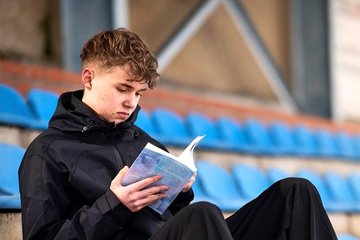 Leon Gabriel Riedel mit seinem Buch auf der Tribüne eines Fußballstadions