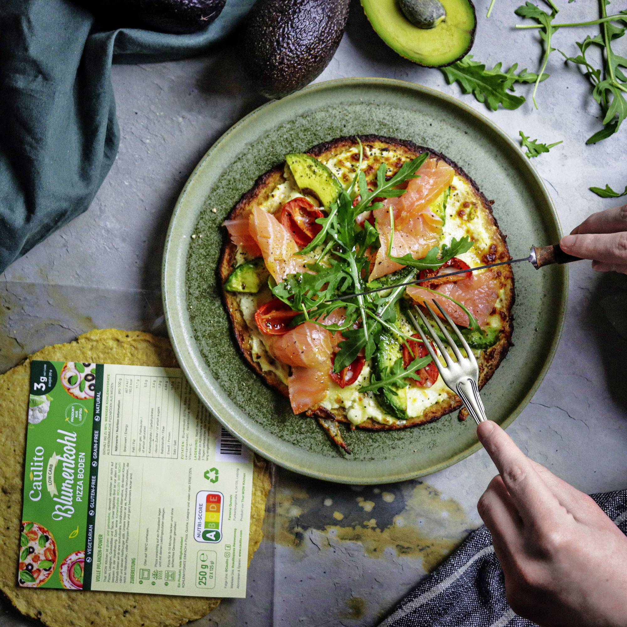 zusehe einen Pizza auf Blumenkohl Basis belegt mit Avocado, Lachs und Rucola 